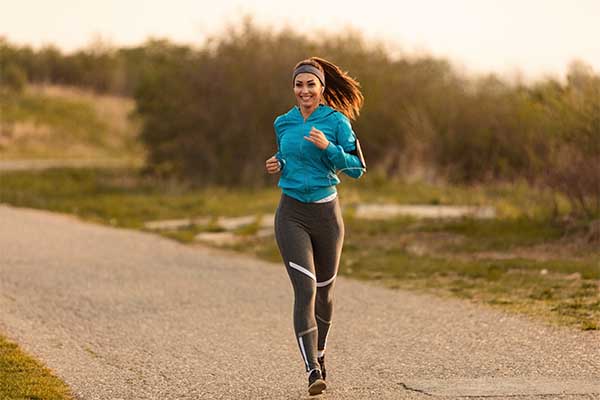 Young happy sportswoman running on the road in the morning