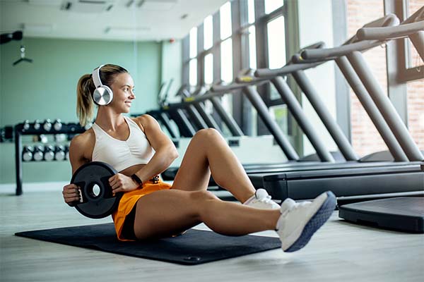 Young female athlete doing Russian Twists exercises with weight plate at health club