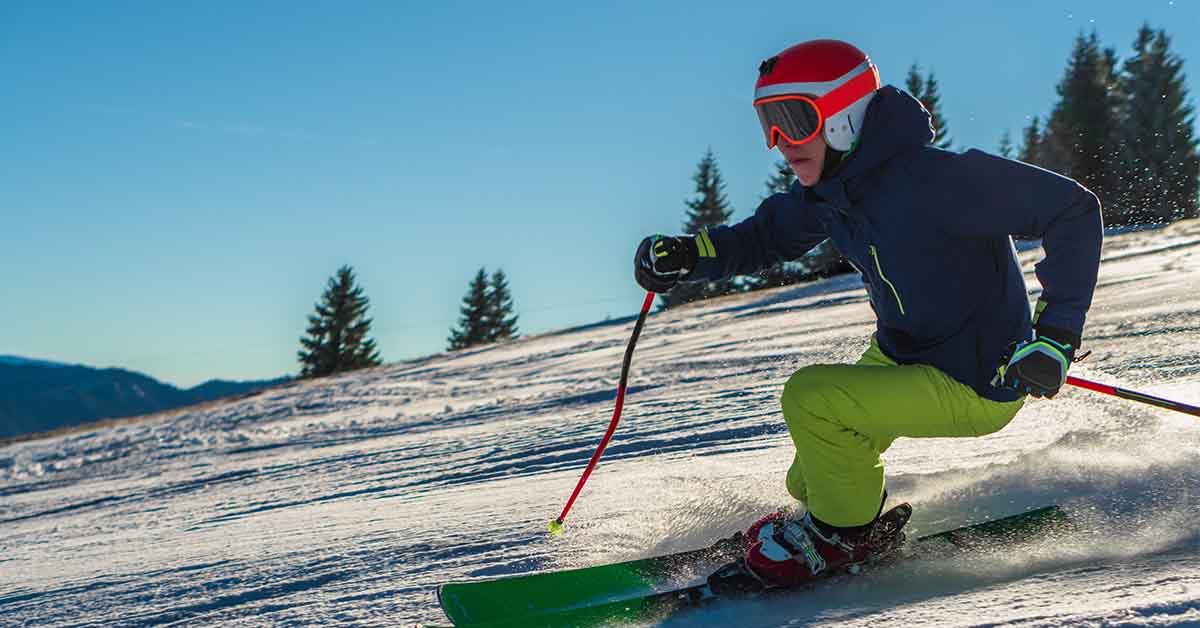 male wearing green pants and bright orange helmet while skiing on a sunny day