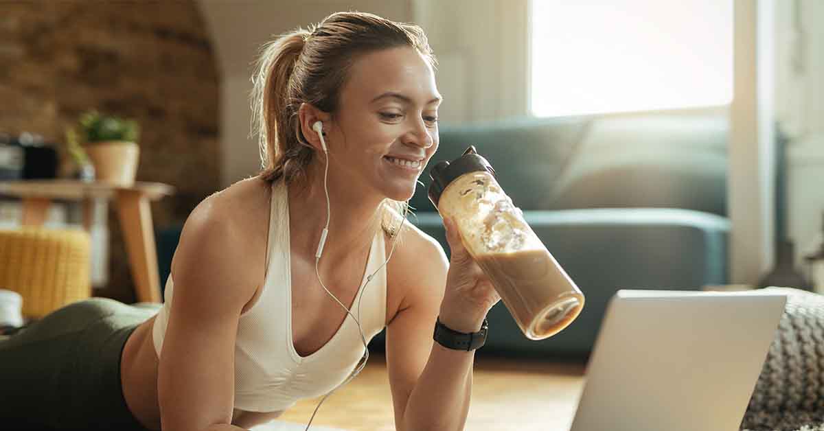 sportswoman drinking smoothie while relaxing on the floor and surfing the net on laptop