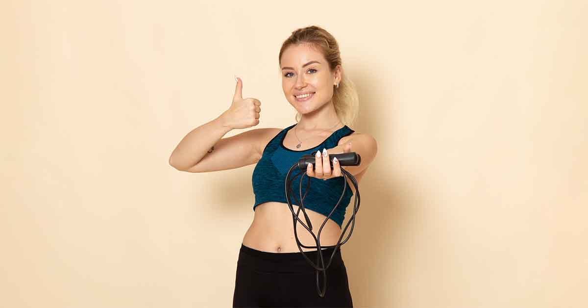 female in sport outfit holding skipping ropes on white wall health beauty workout body sport