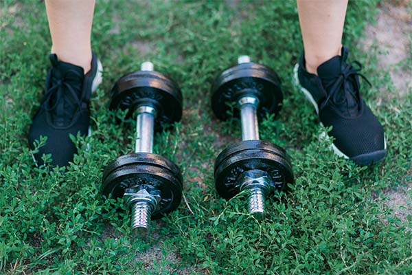 Adjustable Dumbbells on green grass background and feet in black sneakers