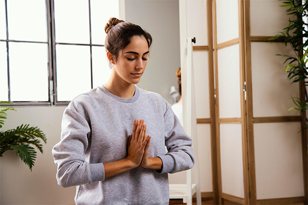 Woman practicing meditation at home with hands in namaste pose for stress management.