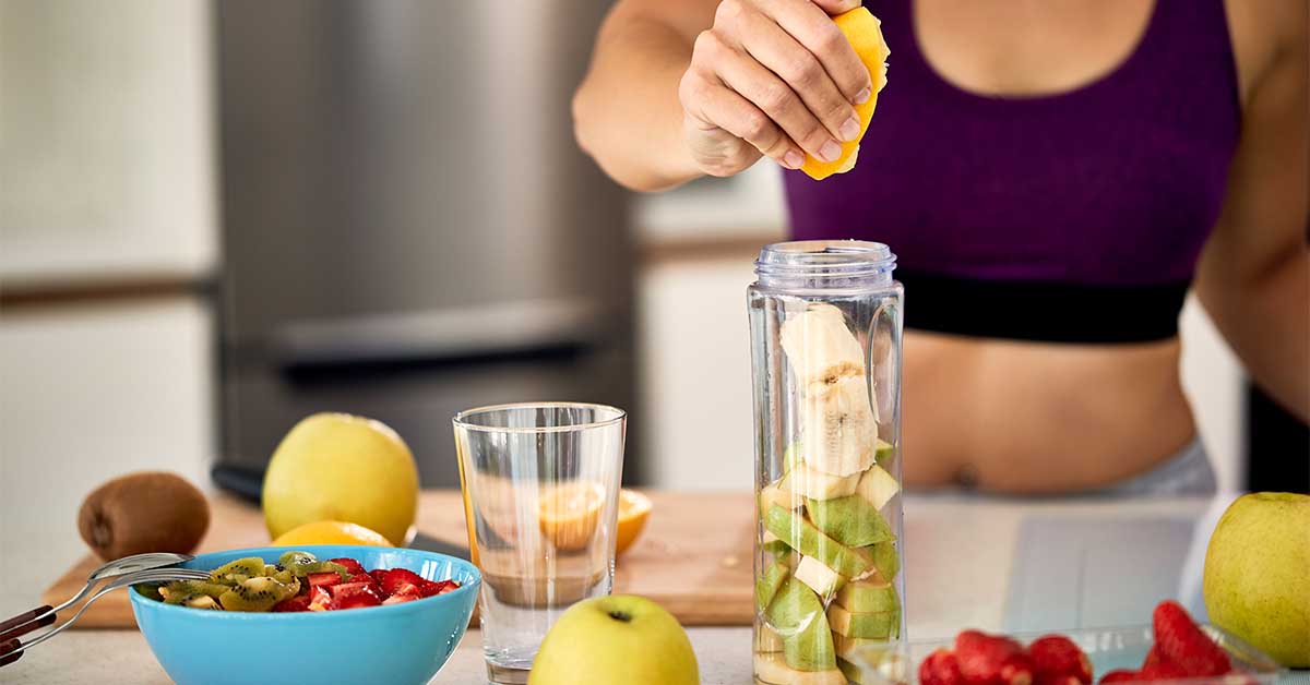 Closeup of sportswoman using lemon while making fruit smoothie at home