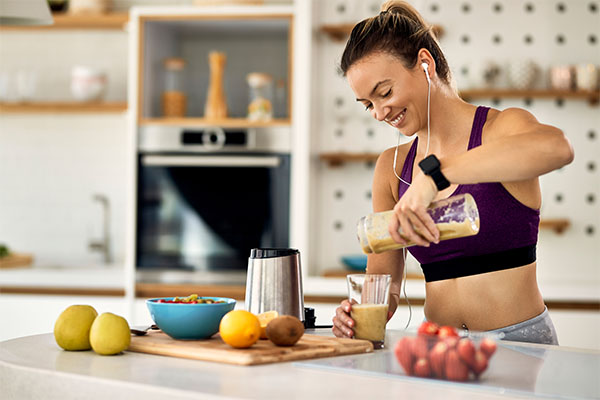 Young happy athletic woman having a fruit smoothie for breakfast